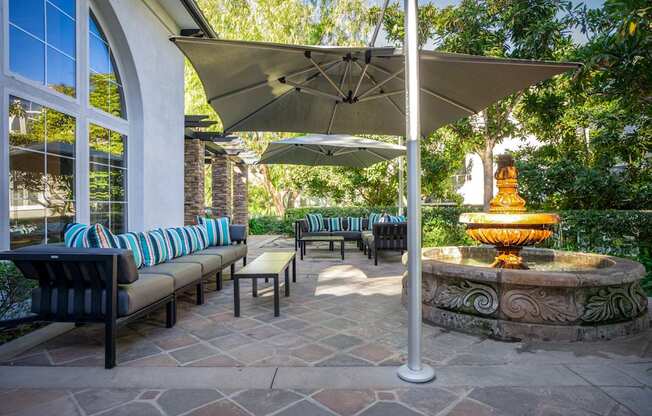 A patio with a fountain and a bench under a canopy.