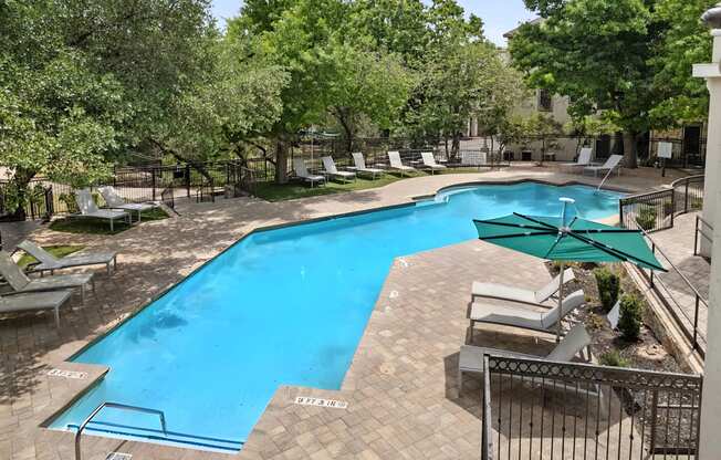 A pool surrounded by trees and lounge chairs.