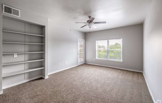 an empty living room with a ceiling fan and a window