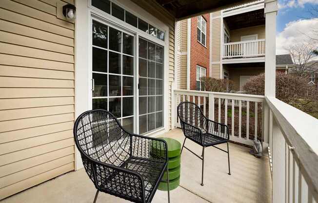 Two black chairs and a green stool are on a porch.