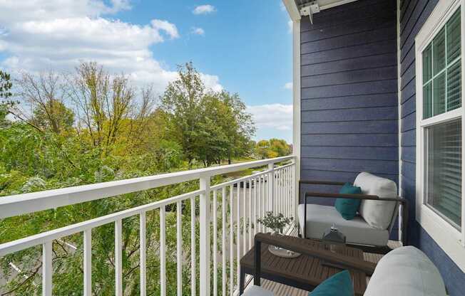 A balcony with a white railing, a brown table, and a white chair with a blue cushion.