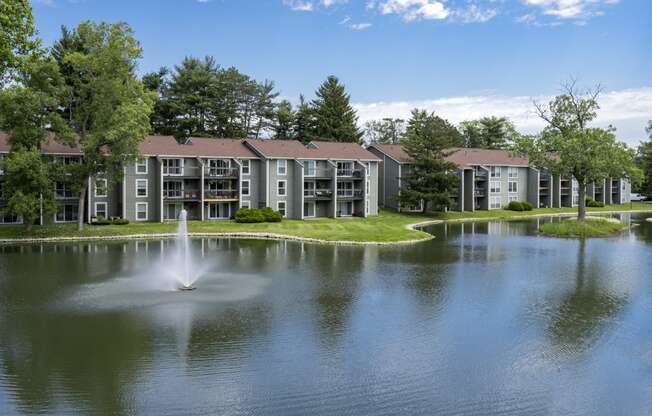 a fountain in the middle of a lake with an apartment building in the background