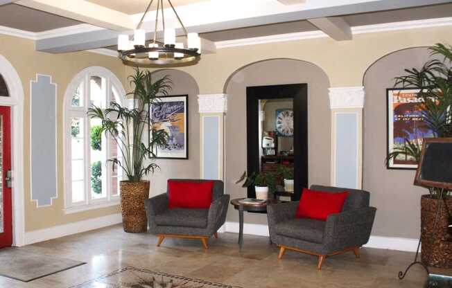 Pasadena Brookmore apartments lobby seating area with large gray midcentury chairs with red pillows on a marble tile floor.