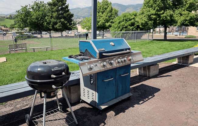 A blue grill is on a picnic table outside.