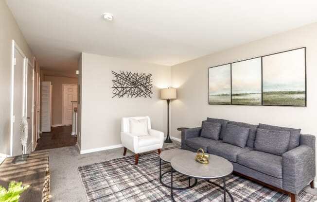 A living room with a grey couch, a white chair, and a table with a golden object on it.