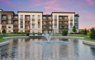 a fountain in a pond with an apartment building in the background