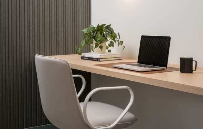A modern office chair is placed in front of a wooden desk with a laptop, a plant, and a black mug on it.