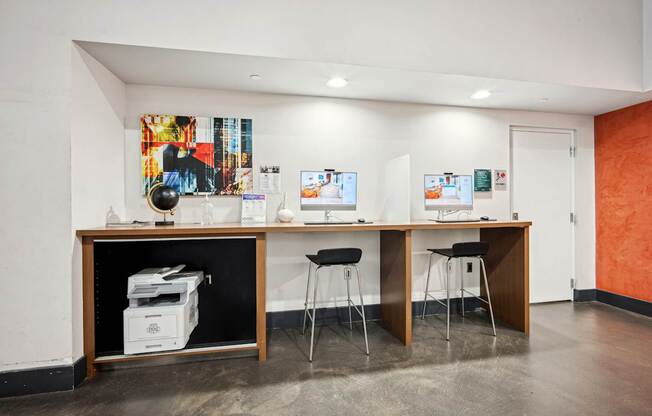 A room with a desk and chairs and a printer on a shelf.