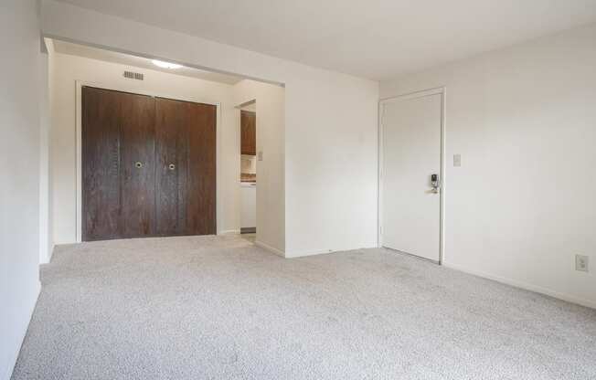 an empty living room with white carpet and a wooden door