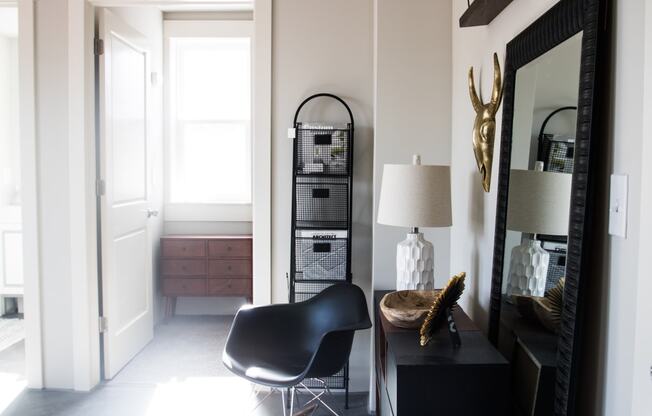 a corner of a room with a chair and a table with a lamp and a large mirror