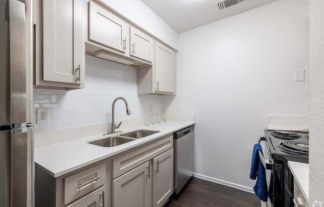 A kitchen with a stainless steel refrigerator, a white sink, and a white countertop.