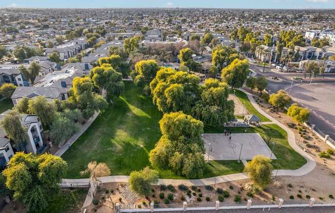 A park with a basketball court surrounded by trees and houses.