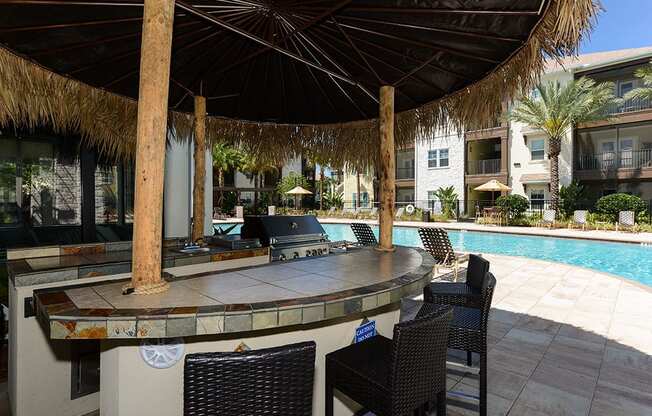 a bar next to a pool with chairs and umbrellas  at Cabana Club - Galleria Club, Jacksonville, 32256