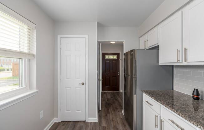 a kitchen with white cabinets and a door to a hallway with a refrigerator