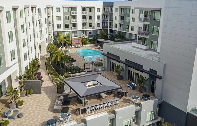 A large outdoor pool area with a table and chairs is surrounded by apartment buildings.