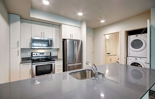 A modern kitchen with a stainless steel refrigerator and a washing machine in the laundry room. at Ravello Apartments, Redmond, Washington