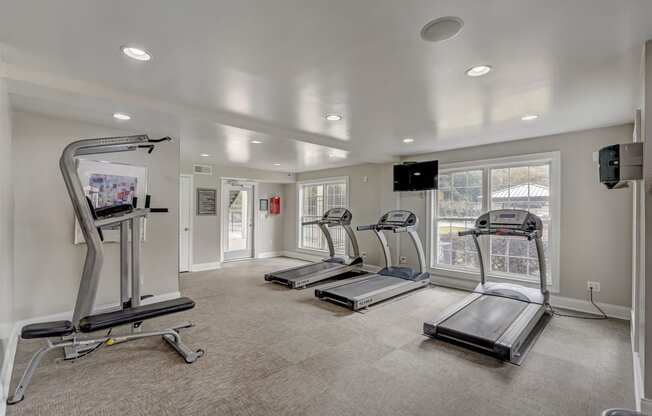 a gym with treadmills and other exercise equipment in a room with windows