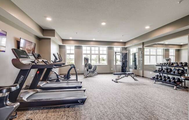 a gym with treadmills and other exercise equipment in a room with windows