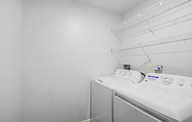 A laundry room with a washer and dryer with a shelf above them at West Hampton Park Apartments in Elkhorn, NE 68022