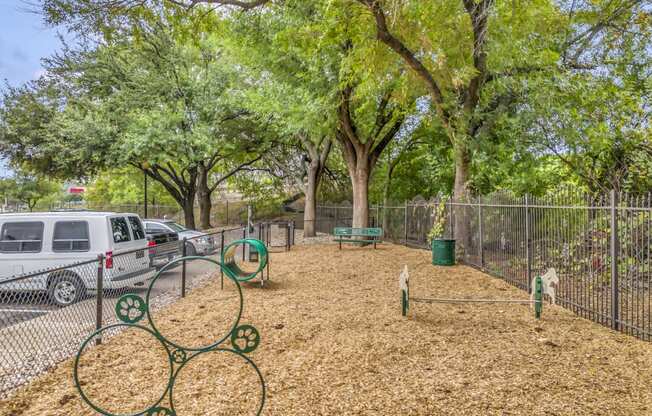 a dog park with trees and a fence and cars parked