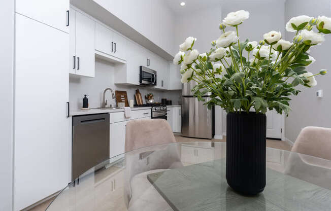 A modern kitchen with a black vase of white flowers on the table.