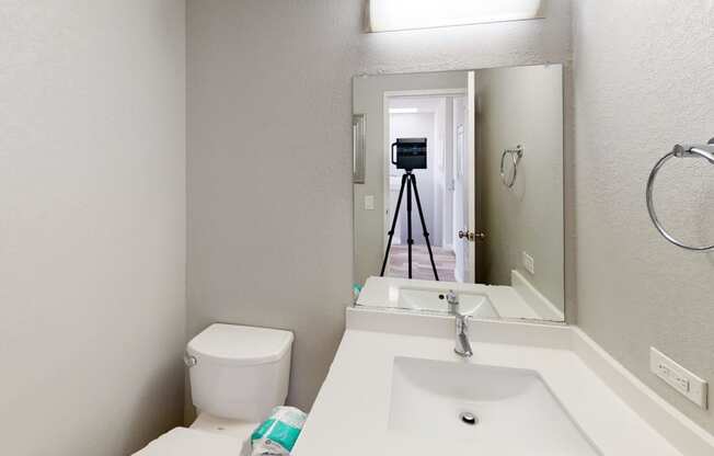 a bathroom with a toilet sink mirror and a camera on a tripod