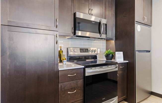 Apartments in Greenwood for Rent - The Morrow Fully-Equipped Kitchen with Stainless Steel Appliances, Dark Cabinetry, Subway Style Backsplash, and Vinyl Plank Flooring