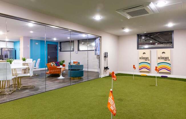 a room with an indoor putting green and a conference room with glass walls