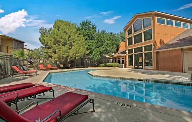 A resort-style swimming pool here at The Bradford with clear blue water, surrounding pool deck, and comfortable lounge chairs for relaxing outdoors. A modern clubhouse and mature trees frame the space, creating a peaceful and inviting community atmosphere.