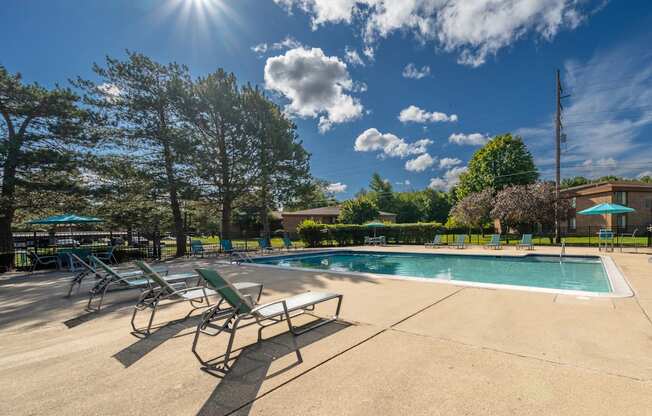 A Heated pool equipped with comfy lounge chairs at Westwood Village Apartments in Westland, MIday at the pool with lounge chairs and trees in the background.
