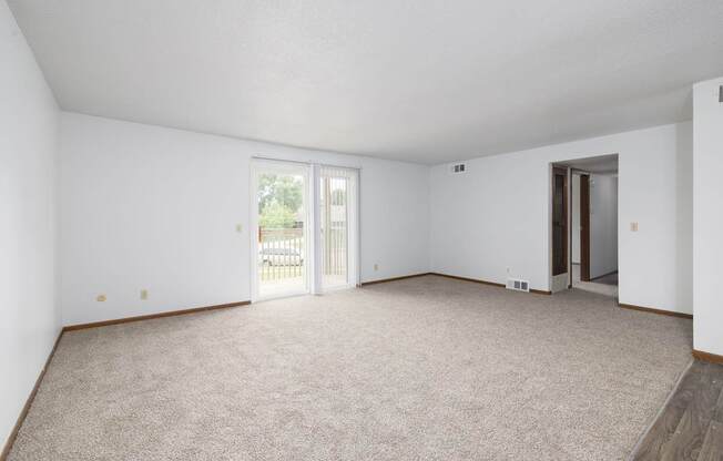 A spacious room with carpeted floor and sliding glass doors.