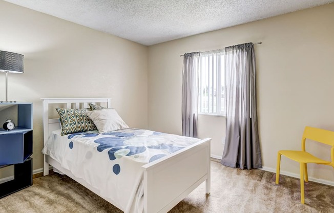 Sunlit bedroom with light curtains and modern flooring in Aurora Meadows apartment.