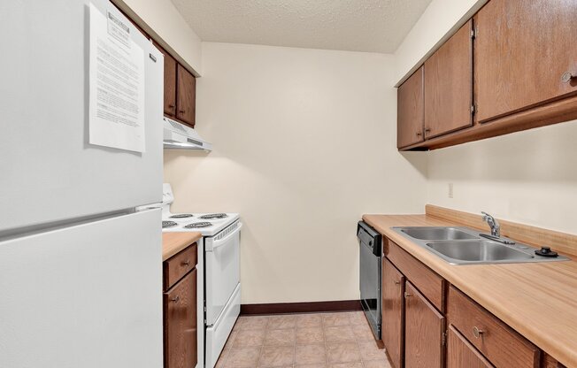 A kitchen with a white fridge, a stove, a dishwasher, and brown cabinets.