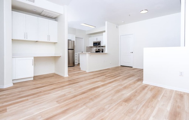 an empty living room with a wood floor and a kitchen