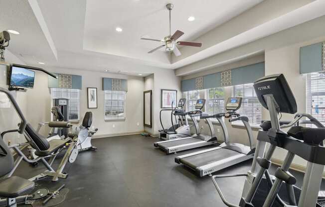 A gym with treadmills, exercise bikes, and a fan.
