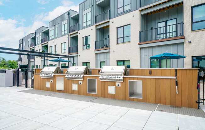 A row of three built-in grilling stations featuring stainless steel gas grills and counters.