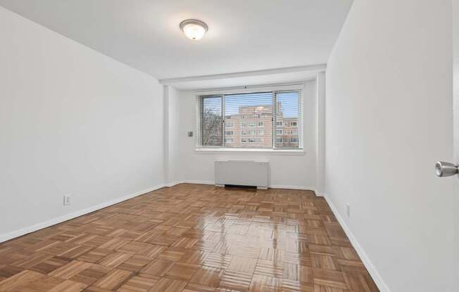A room with wooden flooring and a window overlooking a building.