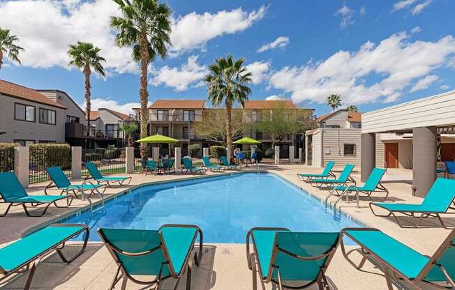 A pool surrounded by lounge chairs and palm trees.