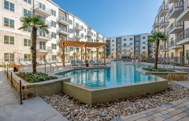A swimming pool surrounded by a stone wall and a wooden pergola.