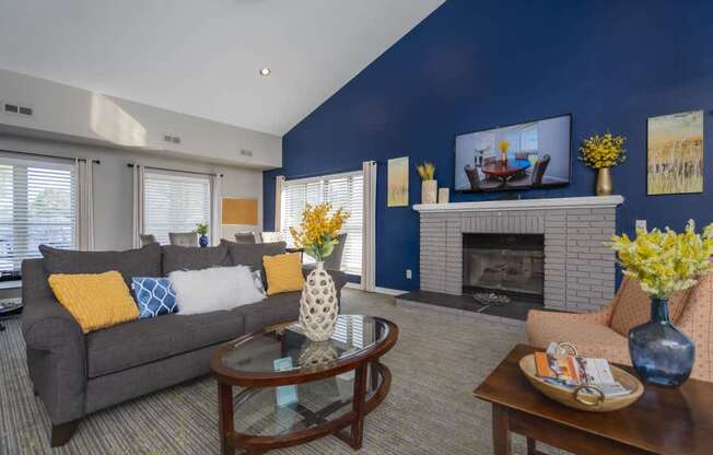 A living room with a grey couch, a glass coffee table, and a fireplace.