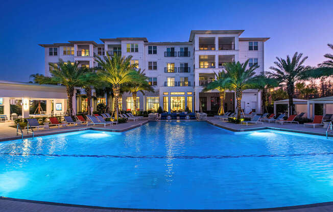 A large, well-lit swimming pool in front of a multi-story residential building.