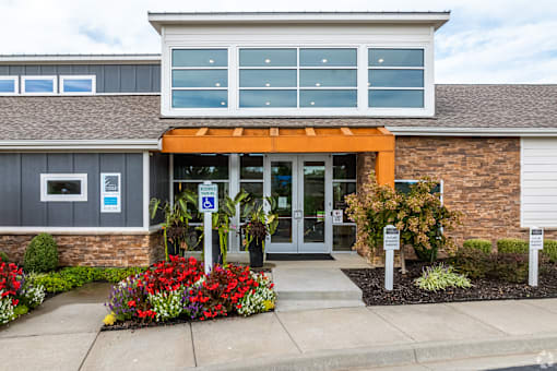 the front entrance of a building with a sidewalk and flowering plants