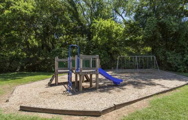 A playground with a blue slide and a wooden structure.