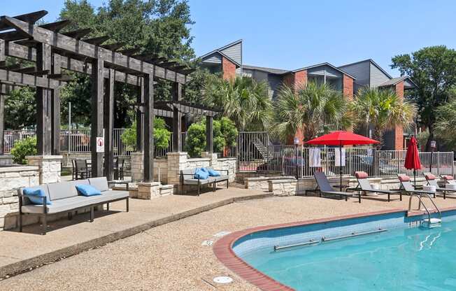 A pool area with a red umbrella and a bench.