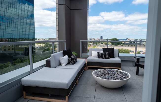 A balcony with two grey cushioned seats and a bowl of stones in the middle.