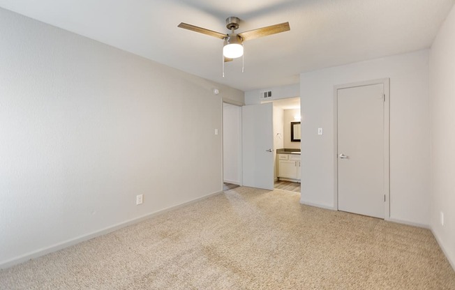 a spacious living room with white walls and a ceiling fan