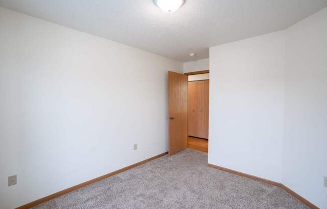 A room with a carpeted floor and a wooden door. Fargo, ND Park Place Apartments