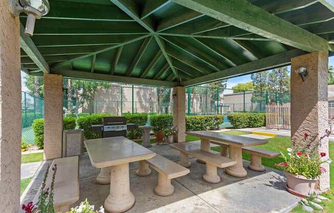 A patio with tables and chairs under a green roof.