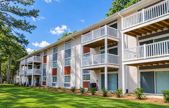 Apartment building with white balcony railings, ground-floor patios and a tree-lined lawn at Icon Avondale Apartments in Decatur, GA.