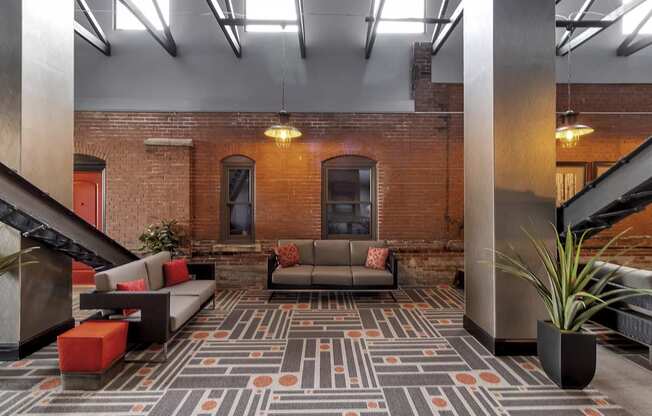 a lobby with couches and a rug in front of a brick wall at The Knights @ 506 Delaware Apartments, Buffalo, 14202